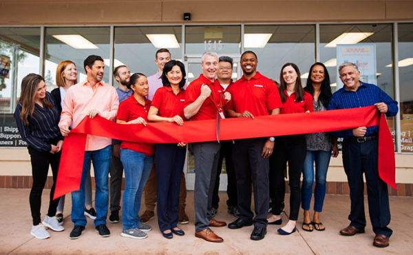 Group of Postnet employees cutting red ribbon celebrating a new store opening. 