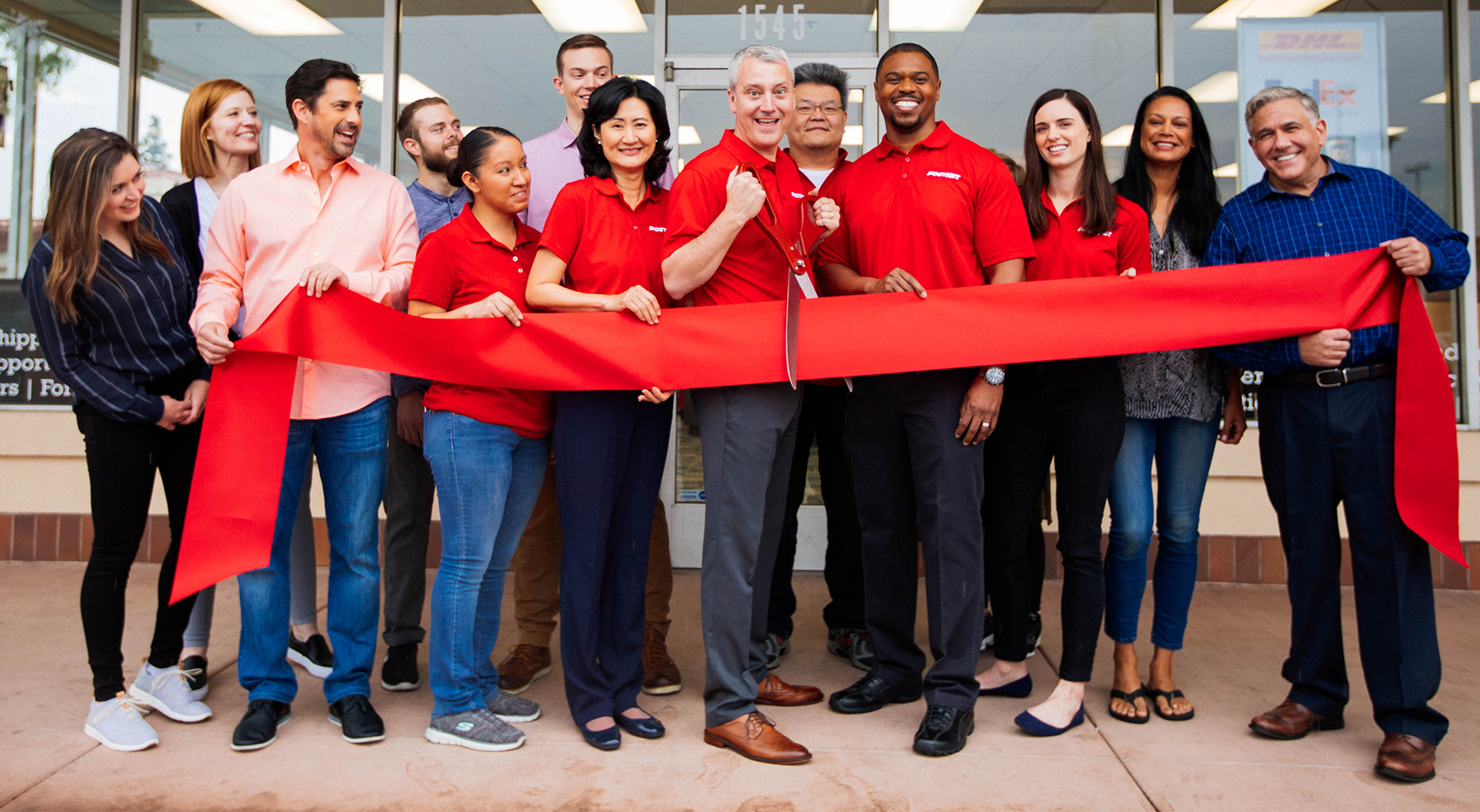 Group of Postnet employees celebrating grand opening and cutting a large red ribbon.