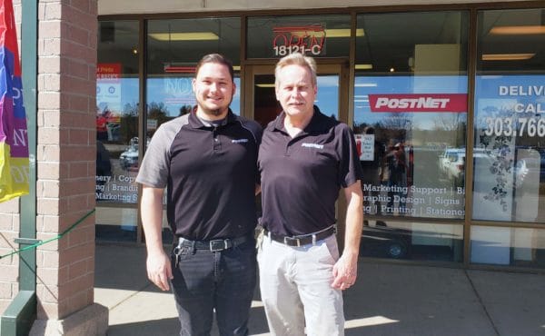 Two franchise owners standing together in front of their Postnet store. 