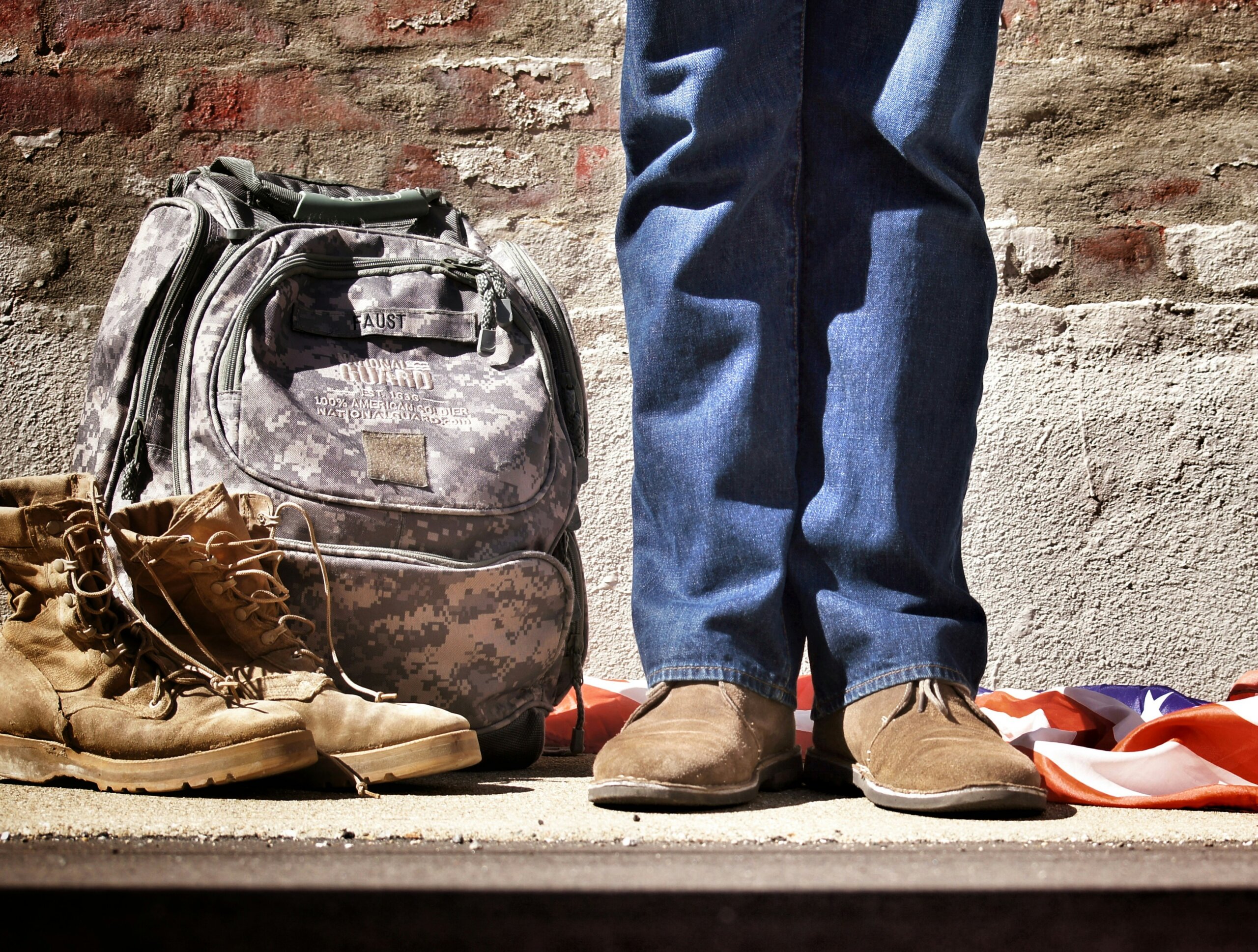 Dark combat boots, camouflage backpack marked "FAUST," person in jeans, folded American flag nearby