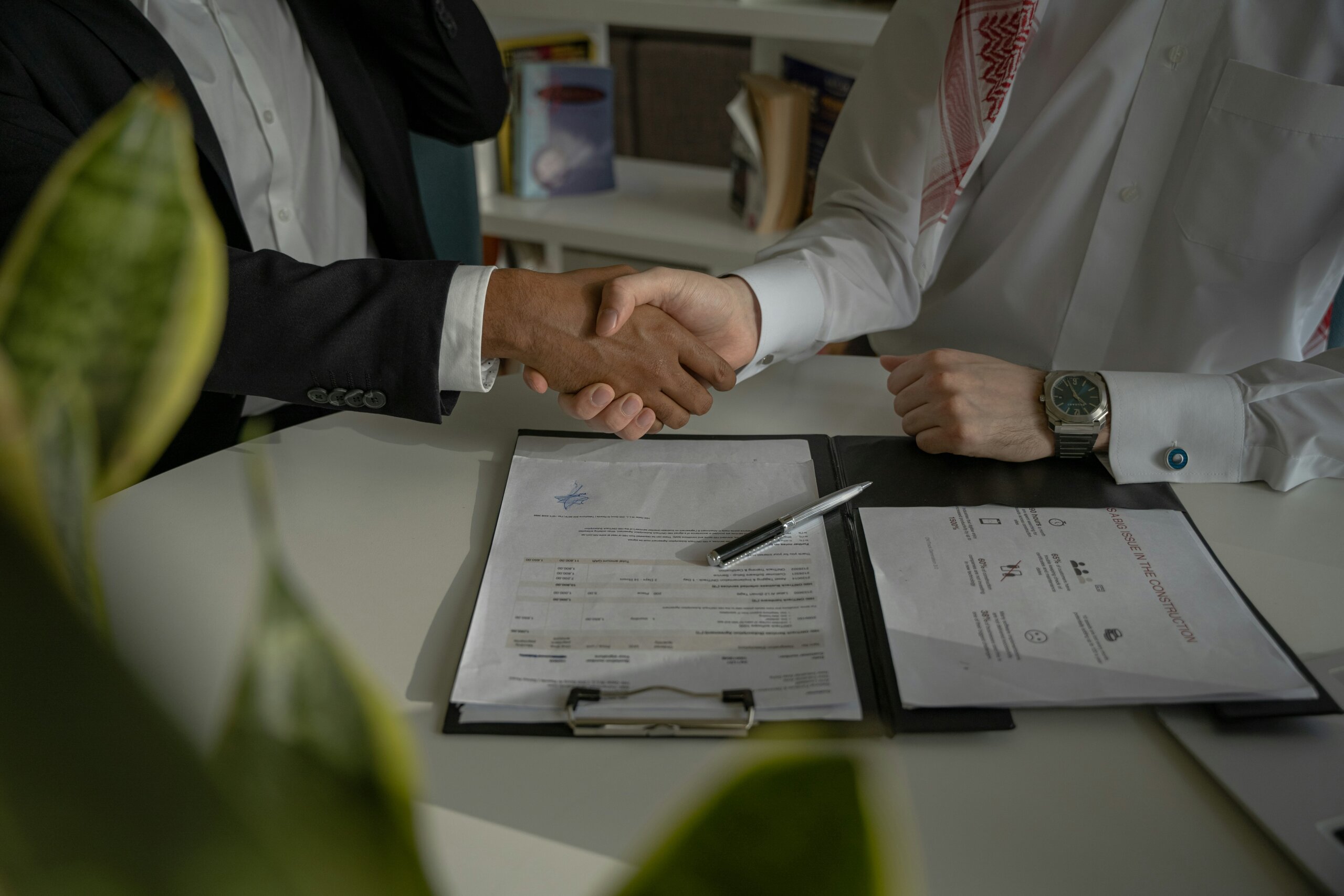 Two people shaking hands over a document on a table